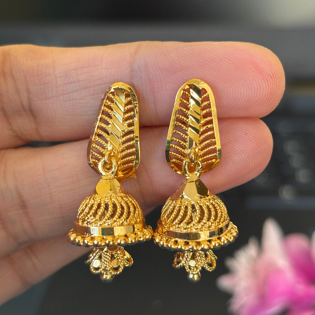 Gold earrings held between fingers with a blurred background