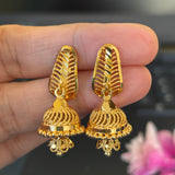 Gold earrings held between fingers with a blurred background
